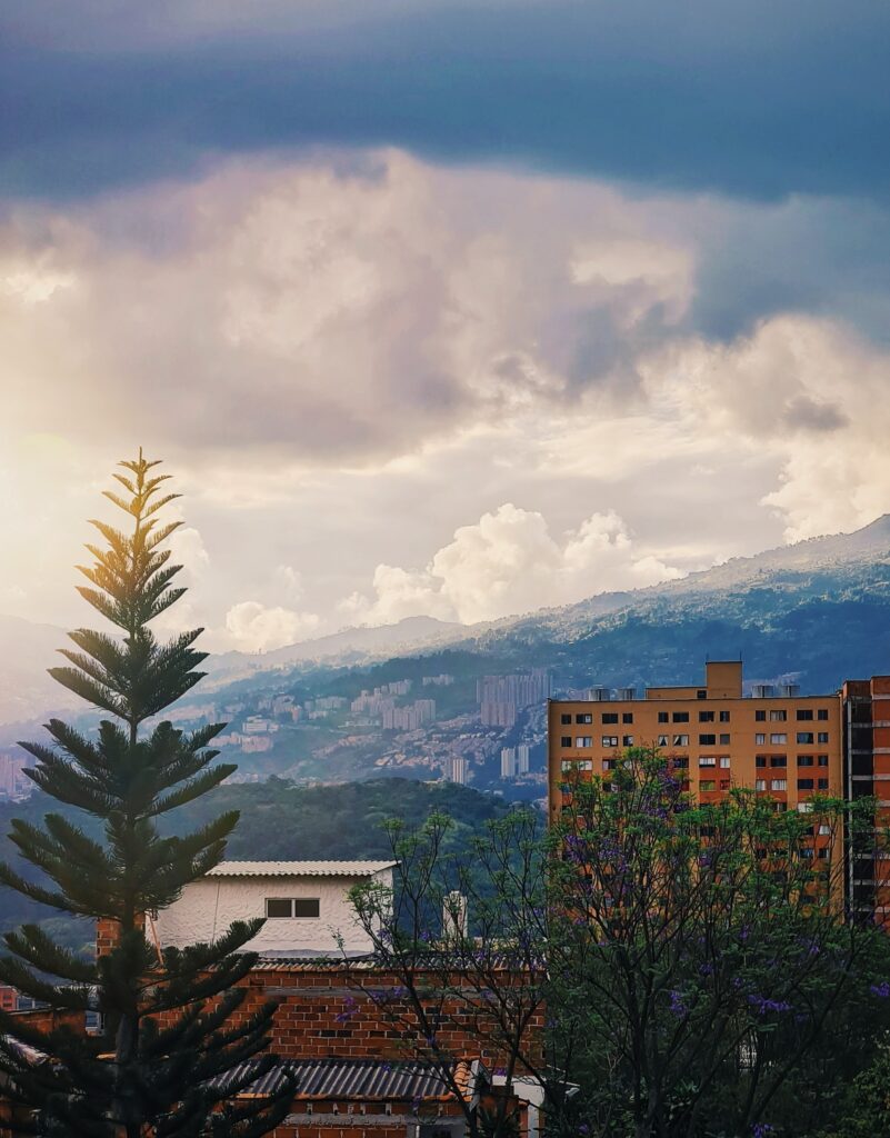 A landscape picture of Medellin that includes a beautiful morning sky, apartment buildings and trees. One of the many scenes you see when you are moving to Colombia.